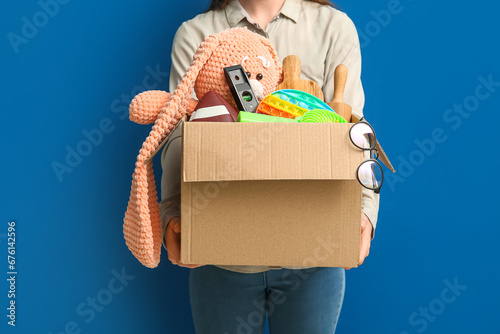 Woman holding box of unwanted stuff for yard sale on blue background photo