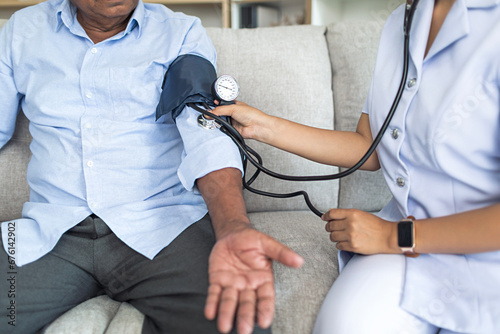Cropped image, Asian female doctor checking old man patient arterial blood pressure at home or nursing home. Health care concept. photo