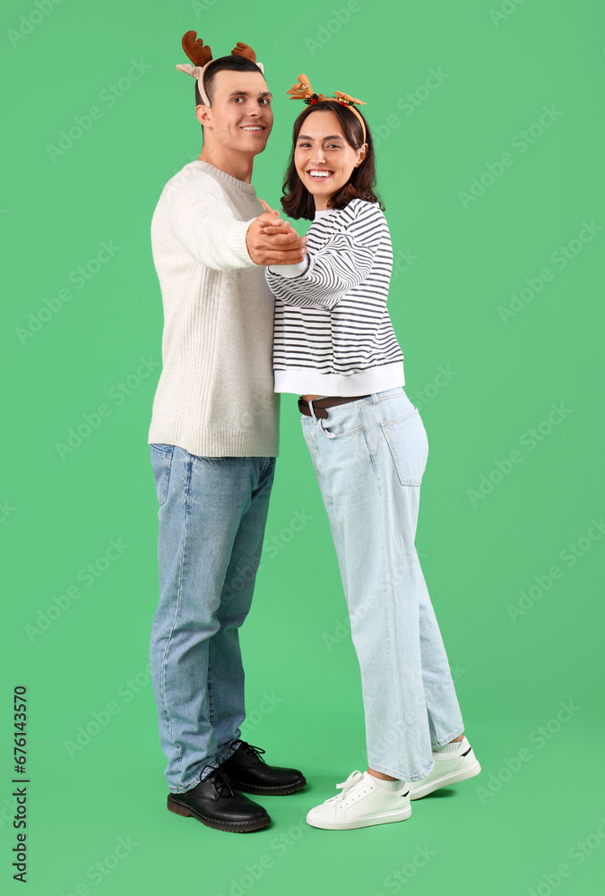 Happy young couple in Christmas reindeer horns hugging on green background Happy young couple in Christmas reindeer horns hugging on green background