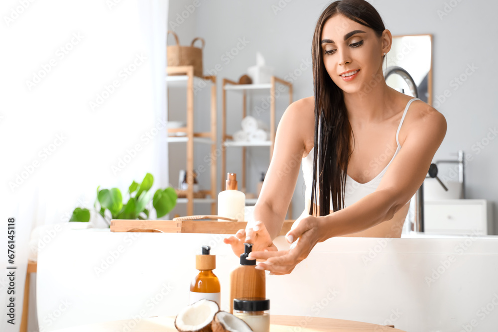 Beautiful young woman applying coconut oil onto her hair in bathroom Beautiful young woman applying coconut oil onto her hair in bathroom