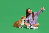 Little girl with cute Corgi dog taking selfie on green background
