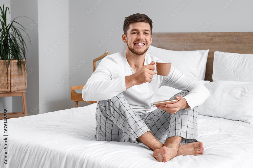 Young bearded man with cup of coffee in bedroom