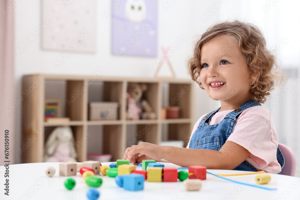 Motor skills development. Little girl playing with wooden pieces and string for threading activity at table indoors Motor skills development. Little girl playing with wooden pieces and string for threading activity at table indoors