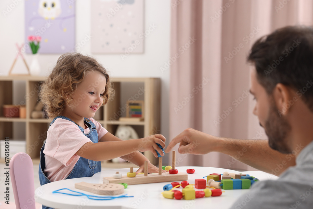 Motor skills development. Father and daughter playing with stacking and counting game at table indoors Motor skills development. Father and daughter playing with stacking and counting game at table indoors