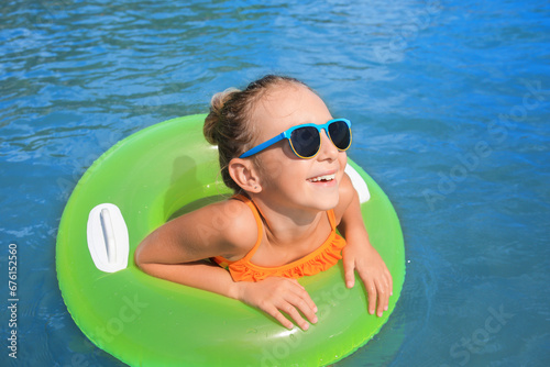 Happy little girl with sunglasses and inflatable ring in sea on sunny day. Beach holiday