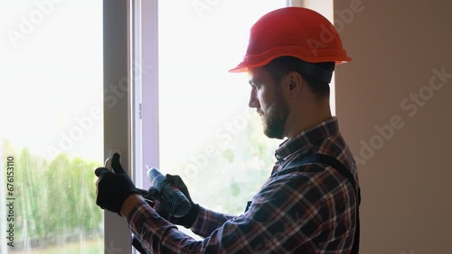 Workman in uniform installing or adjusting plastic windows in the living room at home photo