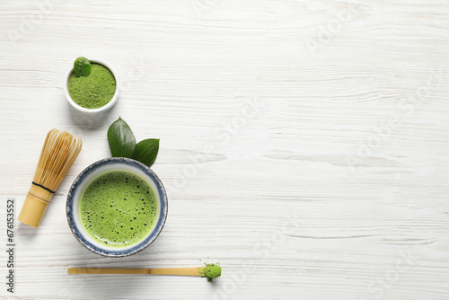 Cup of fresh matcha tea, bamboo whisk, spoon and green powder on white wooden table, flat lay. Space for text