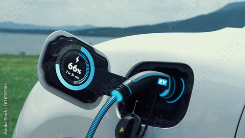Electric car plug in with charging station, recharge battery by EV charger cable display smart digital battery status hologram with nature background. Futuristic green energy infrastructure.Peruse © Summit Art Creations