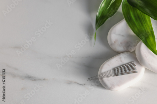 Acupuncture needles, spa stones and green leaves on white marble table, flat lay. Space for text photo