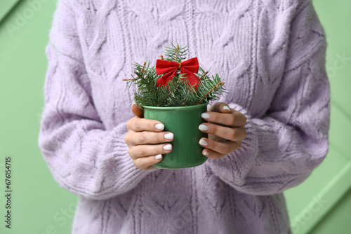 Woman holding cup with beautiful fir tree branches and bow on green background, closeup