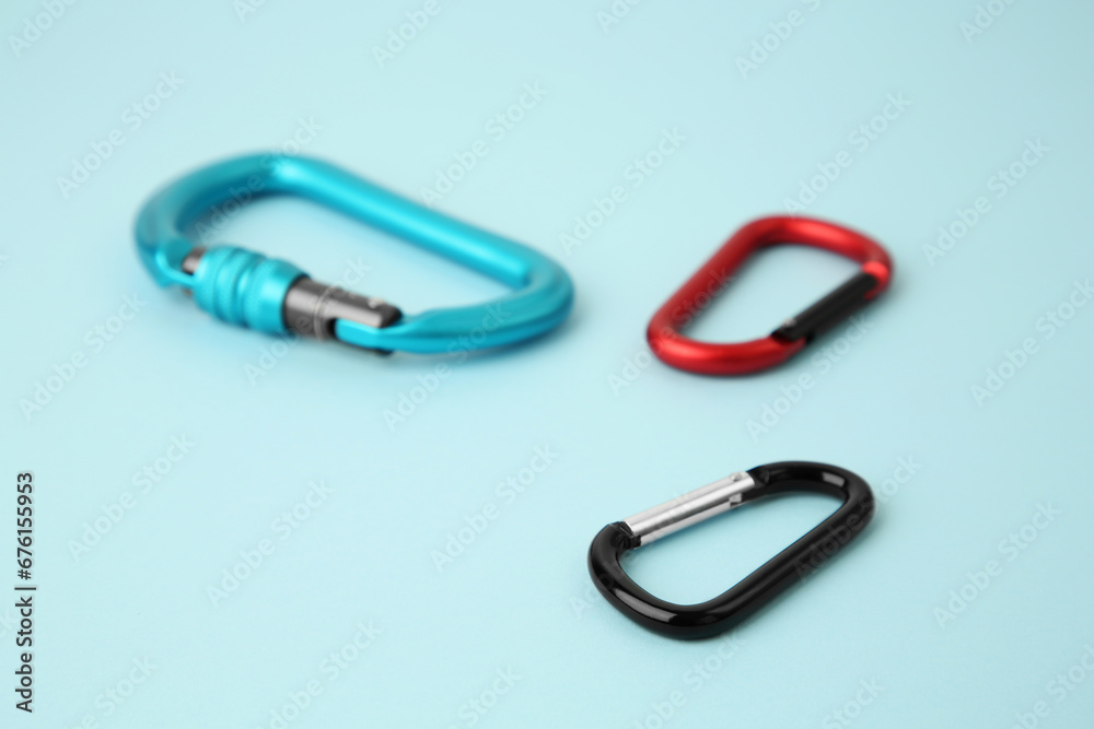 Metal carabiners on light blue background, closeup Metal carabiners on light blue background, closeup