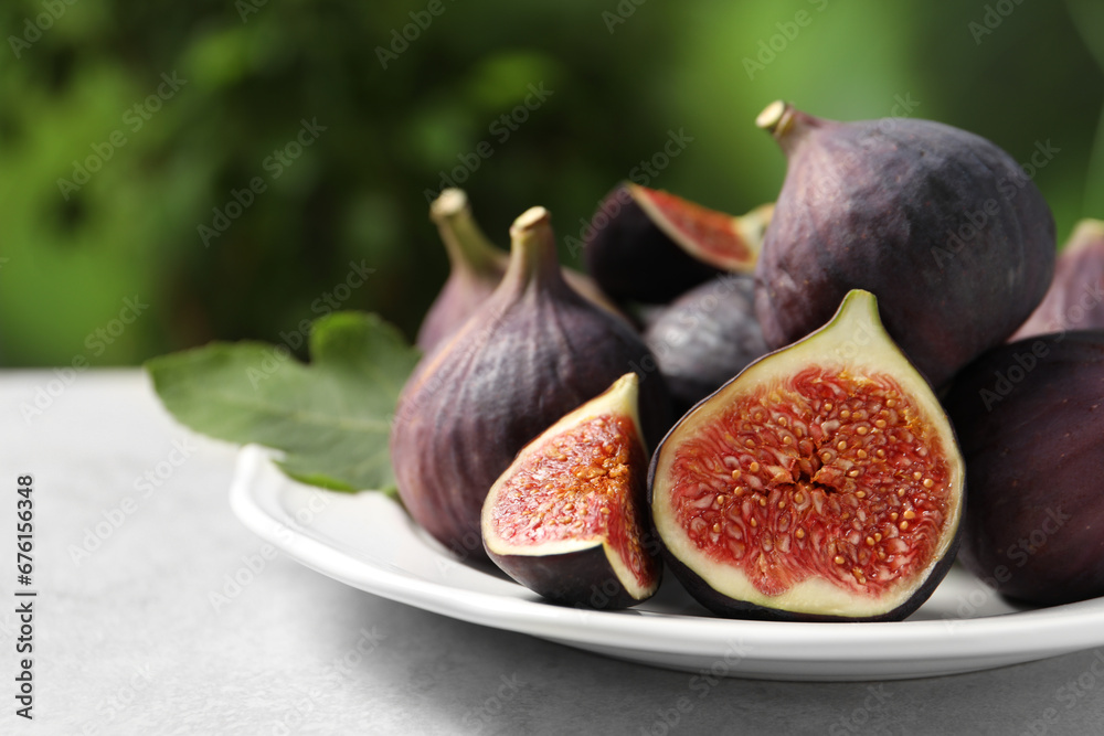 Whole and cut ripe figs on light table against blurred green background, closeup. Space for text Whole and cut ripe figs on light table against blurred green background, closeup. Space for text