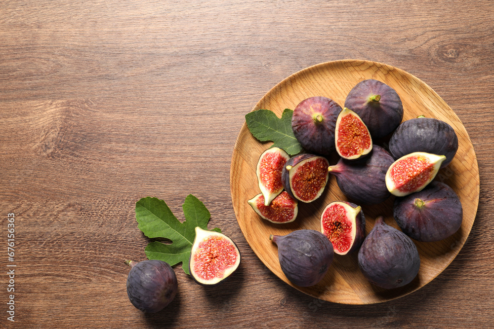 Fototapeta premium Whole and cut ripe figs with leaves on wooden table, flat lay. Space for text