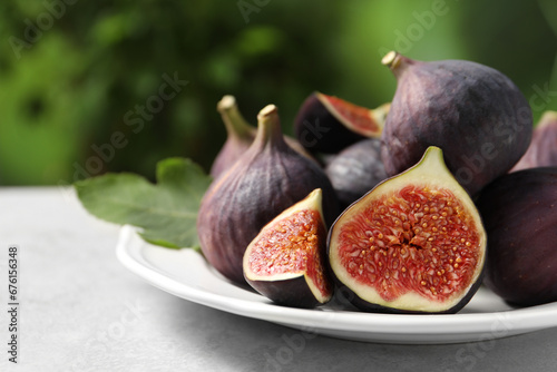 Whole and cut ripe figs on light table against blurred green background, closeup. Space for text