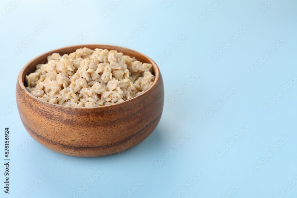 Tasty boiled oatmeal in bowl on light blue background, space for text Tasty boiled oatmeal in bowl on light blue background, space for text