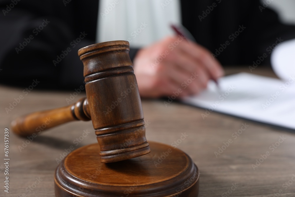 Judge with gavel writing in papers at wooden table, closeup Judge with gavel writing in papers at wooden table, closeup