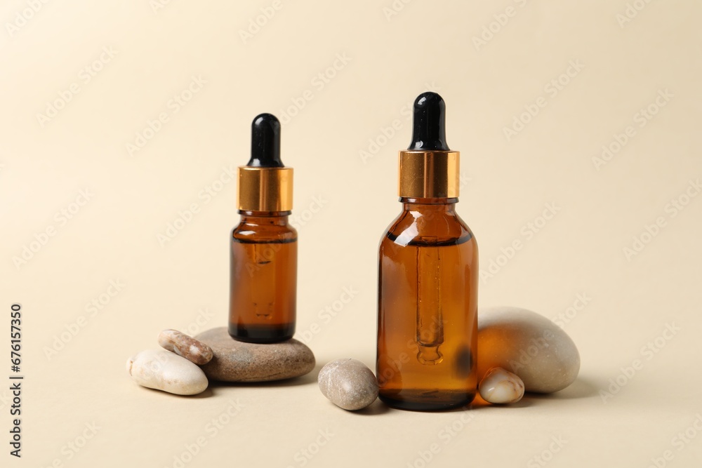 Bottles of cosmetic serum and stones on beige background