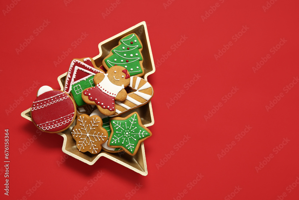 Delicious cookies in Christmas tree-shaped bowl on red background