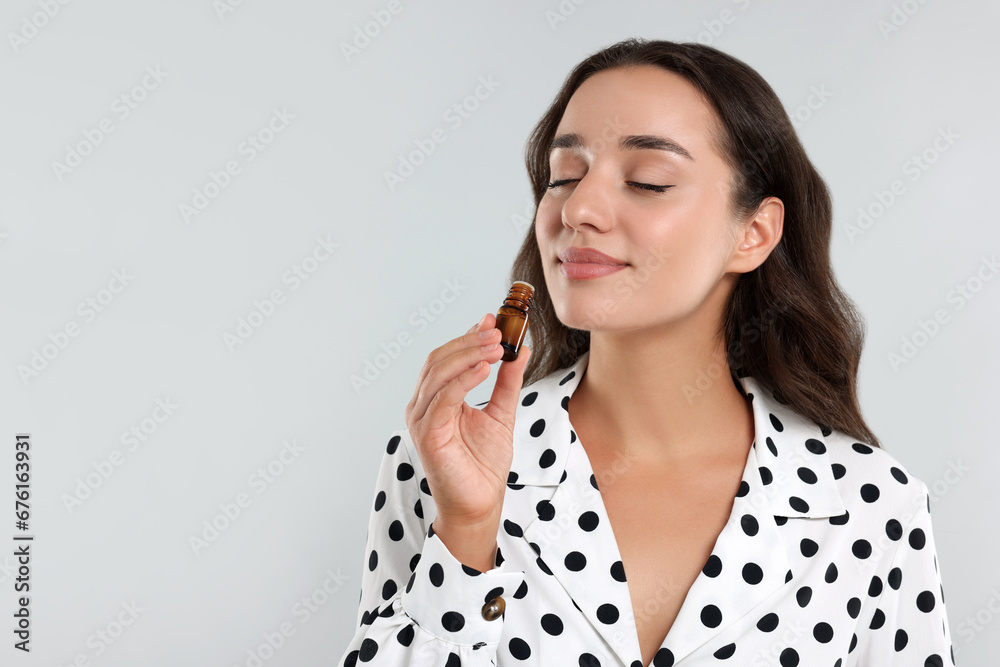 Beautiful young woman with bottle of essential oil on light grey background, space for text - obrazy, fototapety, plakaty 