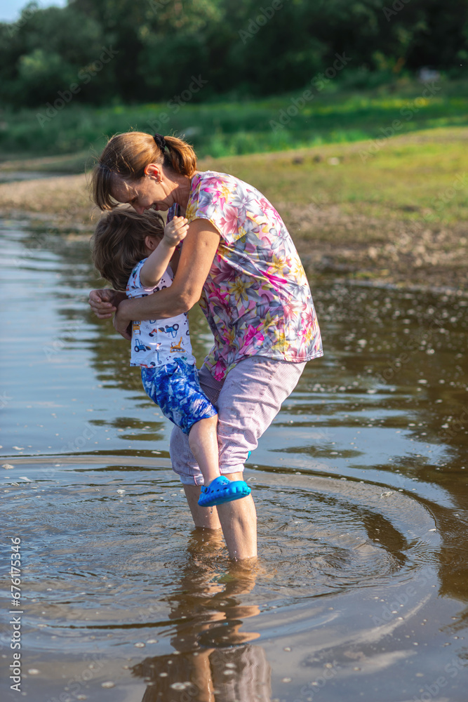 Fototapeta premium Grandson and grandmother playing on the river bank