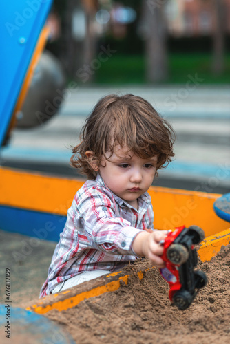 little boy playing in the sandbox with a car