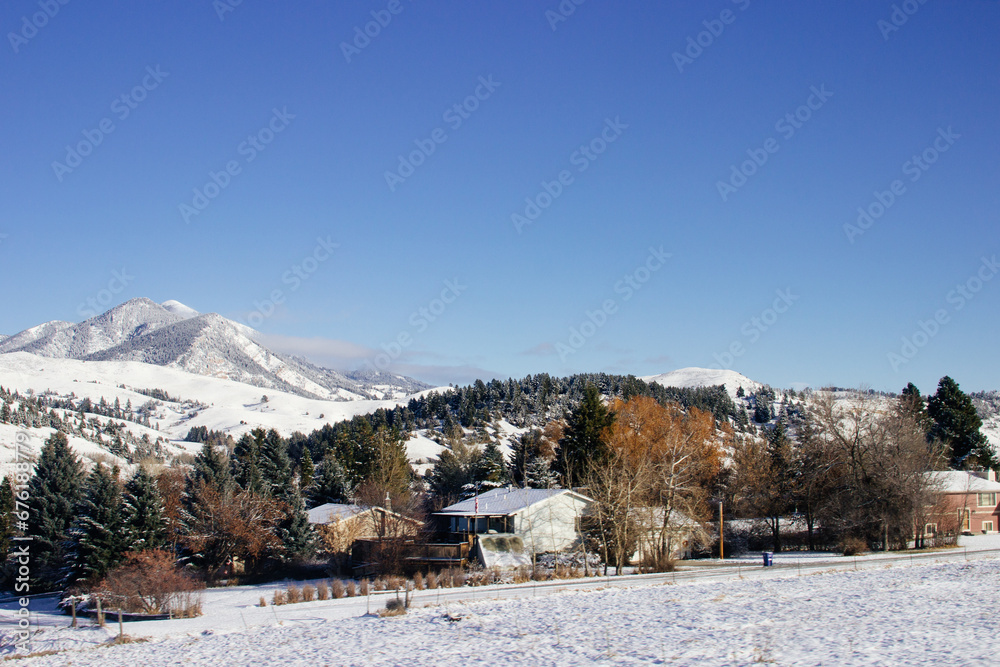 Winter landscape with a snow-covered forest, fir trees on the hills and cozy residential houses. Snow-covered mountains, forests and houses on a sunny winter day