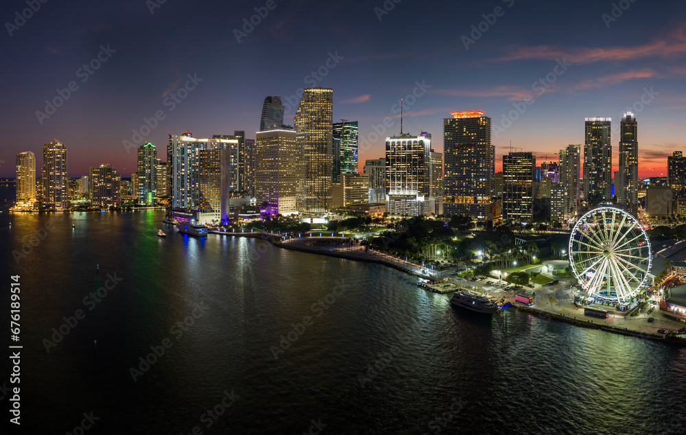 Fototapeta premium Aerial view of Skyviews Miami Observation Wheel at Bayside Marketplace with reflections in Biscayne Bay water and high illuminated skyscrapers of Brickell, city's financial center at night
