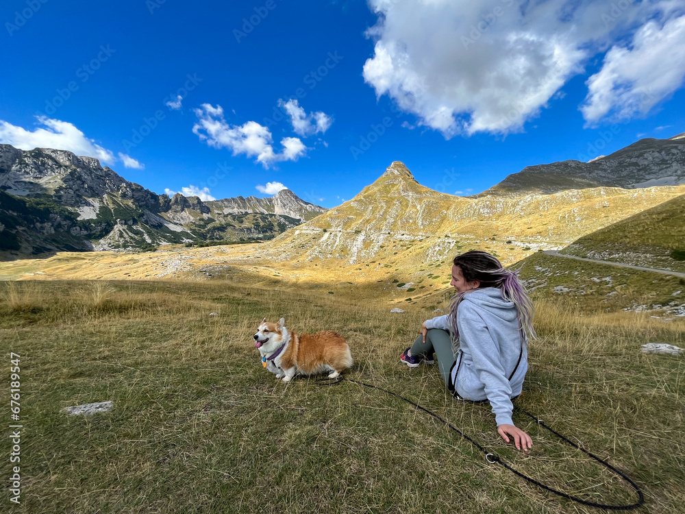 Girl with her bright red dog sitting on a hill high in the mountains