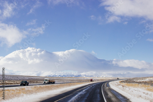 Steep highway among snow-capped mountains on a sunny winter day. Bright blue winter sky with large clouds over an asphalt road. Highways in USA. American roads