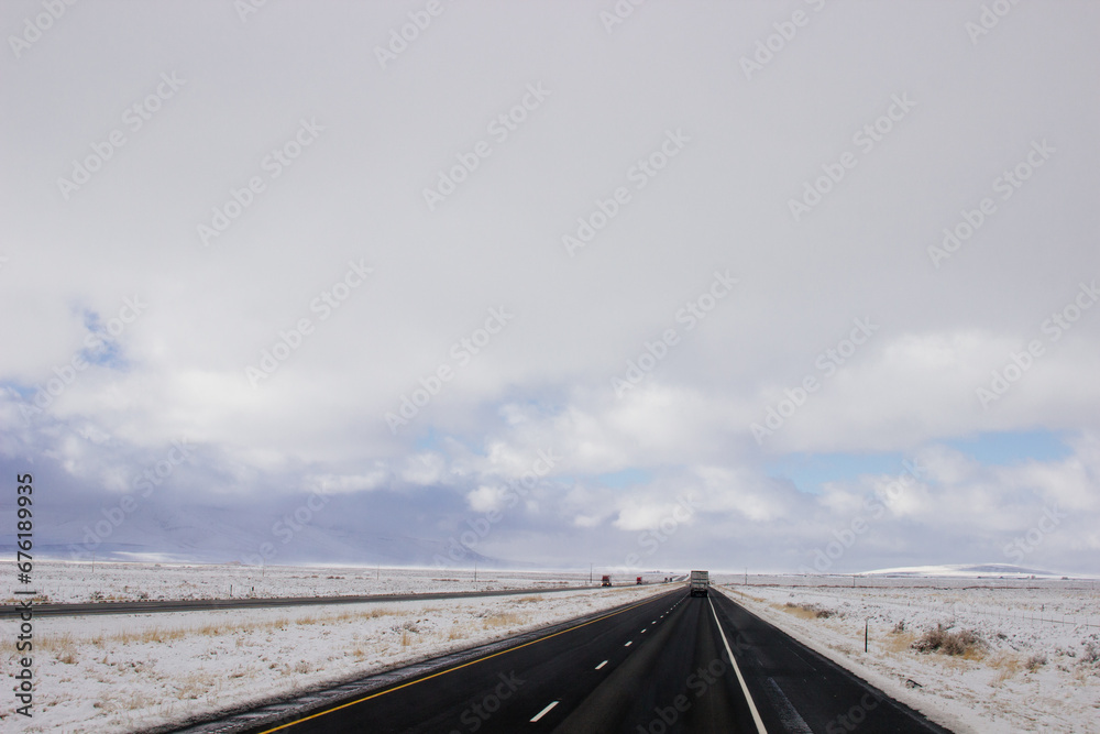 Steep highway among snow-capped mountains on a sunny winter day. Bright blue winter sky with large clouds over an asphalt road. Highways in USA. American roads