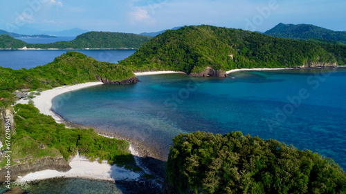 Tropical island with a sandy beach and jungle. Aerial view of a tropical island's hilly coastline, lagoon, beach and tropical rainforest.