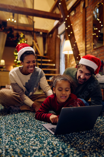 Happy black girl using laptop while spending Christmas eve with her parents at home.