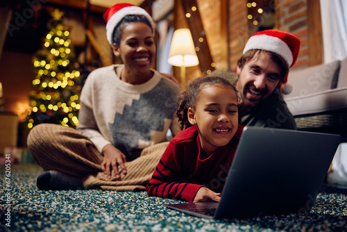 Happy multiracial family surfing the net on laptop at home on Christmas. © Drazen