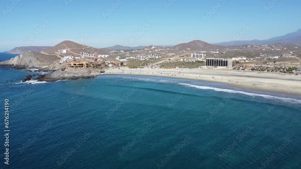 Aerial shot over the beautiful resort of cerritos beach in mexico with a view of the turquoise sea with calm waves, hotel buildings, many beachgoers and dry landscape on a cloudless day Aerial shot over the beautiful resort of cerritos beach in mexico with a view of the turquoise sea with calm waves, hotel buildings, many beachgoers and dry landscape on a cloudless day
