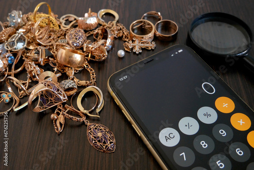 Pawnshop concept, calculator, a lot of gold jewelry and a magnifying glass on a dark wooden table, top view,