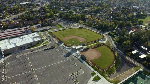 Dolly in aerial drone wide shot approaching empty baseball diamond fields from above behind an American high school surrounded by colorful trees and houses on a sunny fall day in Utah photo