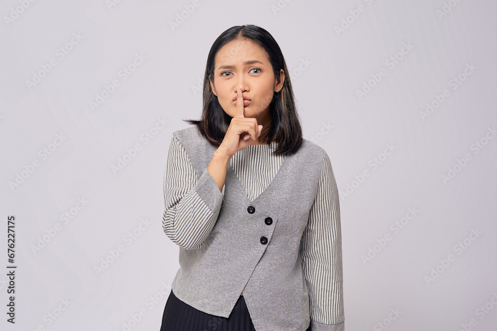 Unhappy young Asian woman in casual clothes makes a silence gesture with a finger and asks to be quiet with serious expression isolated on white background. People lifestyle emotion concept Unhappy young Asian woman in casual clothes makes a silence gesture with a finger and asks to be quiet with serious expression isolated on white background. People lifestyle emotion concept