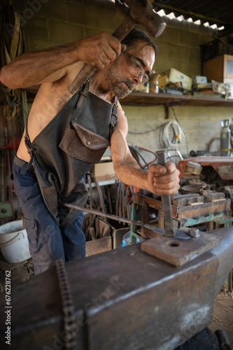 Overview of a blacksmith striking a piece of steel on a anvil.