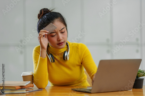 Young Asian woman with headphones around her neck is using a banking application to buy or pay for mobile services online but her credit card is not approved. Unable to get data on laptop. photo