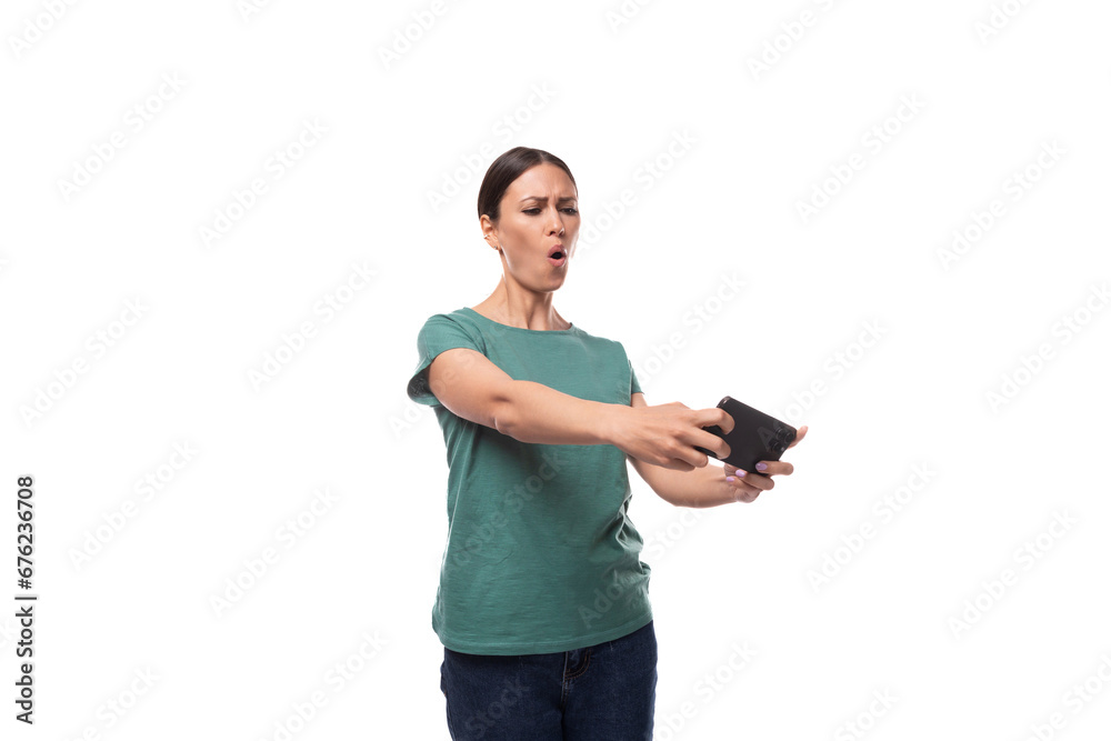 well-groomed young brunette woman dressed in a green t-shirt and jeans plays a game on the phone well-groomed young brunette woman dressed in a green t-shirt and jeans plays a game on the phone