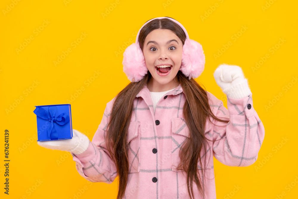 surprised kid in earmuffs and mittens hold gift box on yellow background, giftbox surprised kid in earmuffs and mittens hold gift box on yellow background, giftbox
