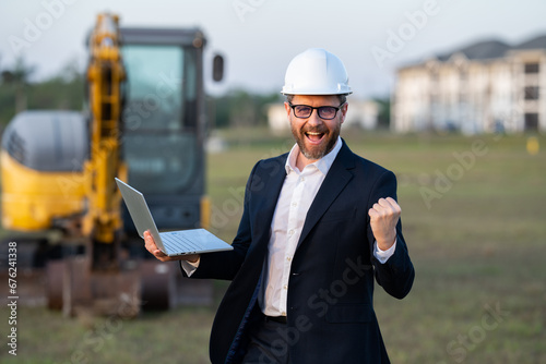 Civil engineer worker at a construction site. Engineer man in front of house background. Confident engineer worker at modern home building construction. Hispanic civil engineer in helmet.