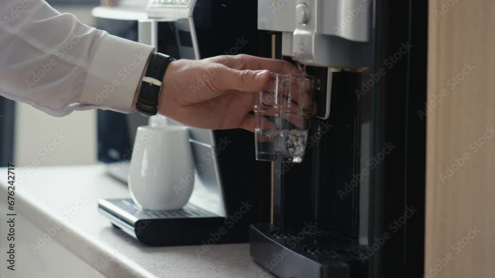 Midsection side shot of unrecognizable office worker pouring still water into glass cup from water dispenser in office Midsection side shot of unrecognizable office worker pouring still water into glass cup from water dispenser in office