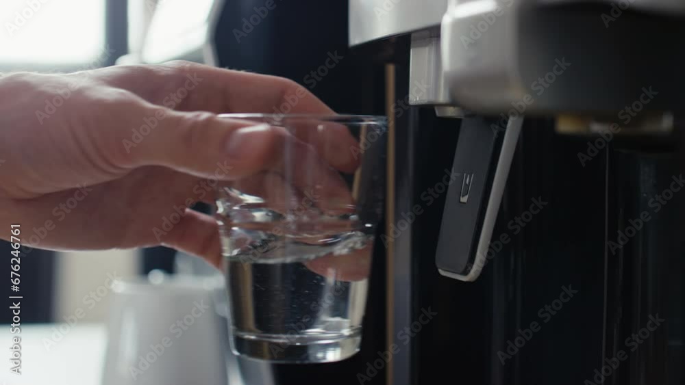 Close up side shot of hand of unrecognizable male office worker with watch pouring fresh water from water dispenser into glass during workday in office Close up side shot of hand of unrecognizable male office worker with watch pouring fresh water from water dispenser into glass during workday in office