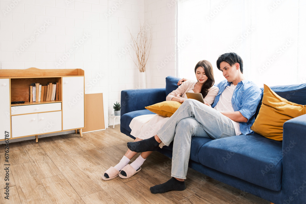 An attractive married man holding a tablet and a woman sit on the floor together in the living room looking at the camera at the new home. A family spends quality time together after home moving.
