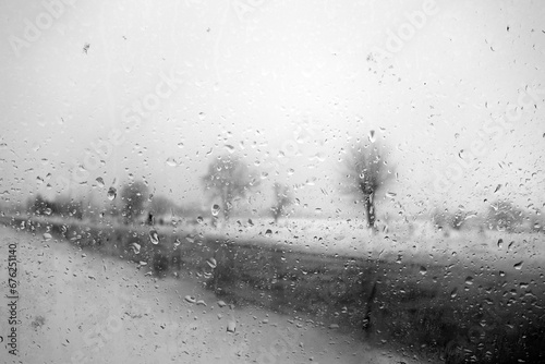 View on winter road and trees through wet windshield with rain drops. Black and white