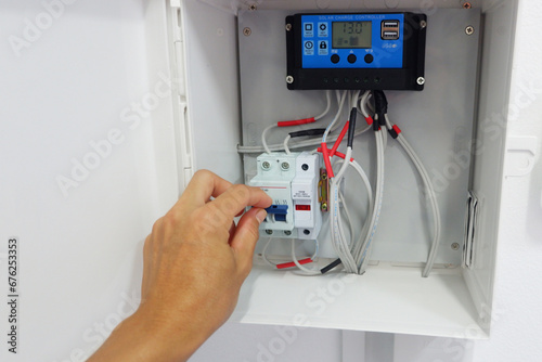 Man's hand showing the installation of a solar charger and circuit breaker in a cabinet for a solar cell system.