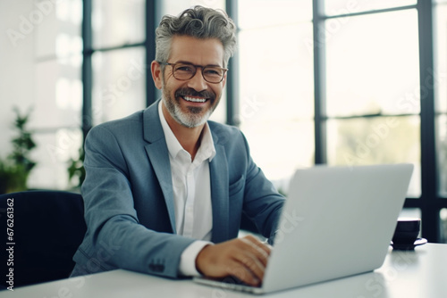 Senior software developer working on a laptop in an office, Mature business man looking at the camera while sitting at his desk, Happy business professional working in tech