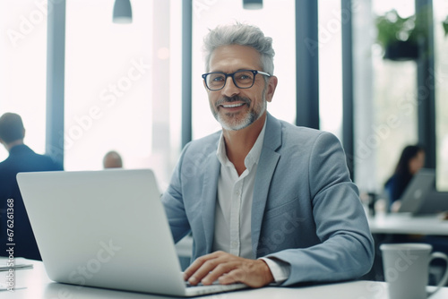 Senior software developer working on a laptop in an office, Mature business man looking at the camera while sitting at his desk, Happy business professional working in tech