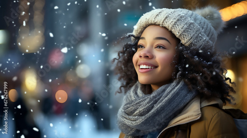 Mujer afroamericana de pie con gorro blanco de lana y sonriendo en un día que esta nevando en la ciudad. Mujer afroamericana sonriendo viendo caer nieve.